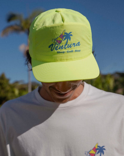 A person wearing a lime cap featuring a colorful sailboat and palm tree logo on the front.