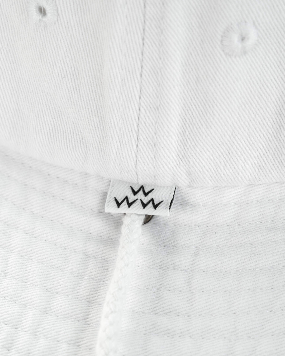Detail of white cotton boonie featuring a small label with a black W motif and a drawstring.