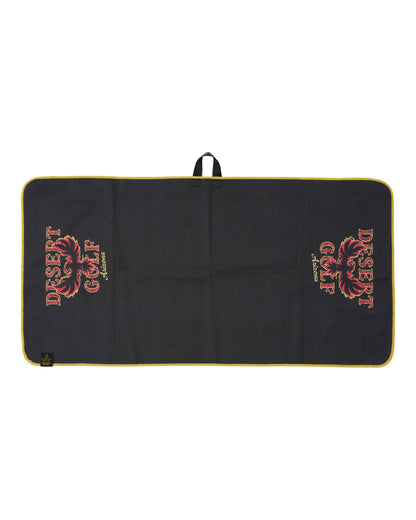 A black rectangular golf towel with a yellow border, featuring the 'Desert Golf' logo printed in red and gold on both sides. 