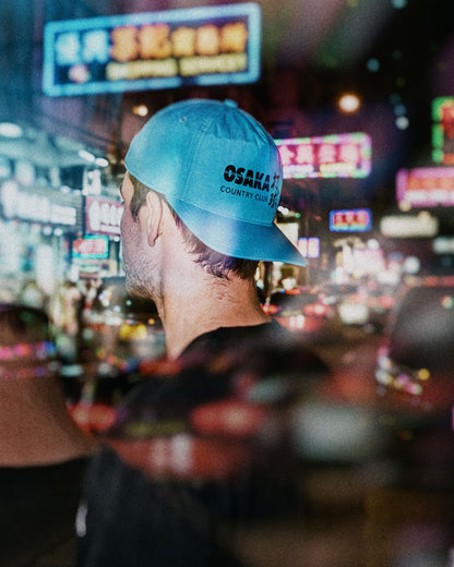 Electric blue snapback hat featuring black Osaka Country Club text printed on the side panel.