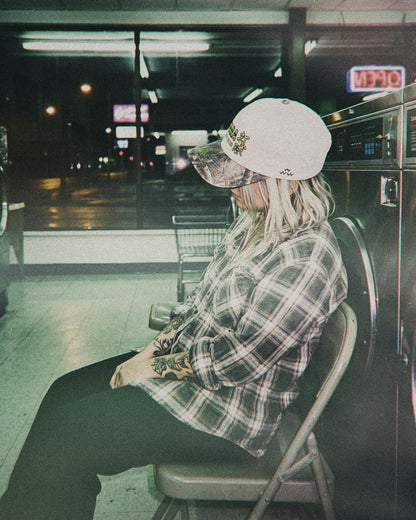 A person sitting indoors wearing a natural snapback with a camouflage print brim and gold embroidery.