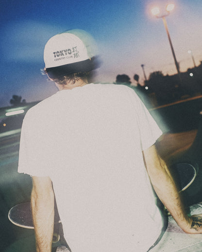 A person from behind wearing a white snapback with a black brim and a Tokyo Country Club front logo.