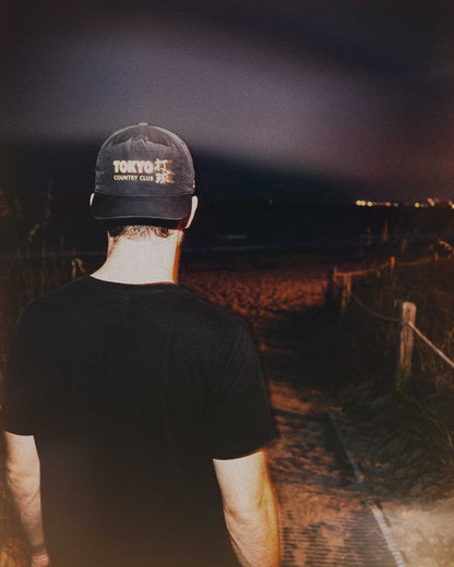 A person wearing a black snapback cap featuring a yellow graphic on the front, viewed from behind.