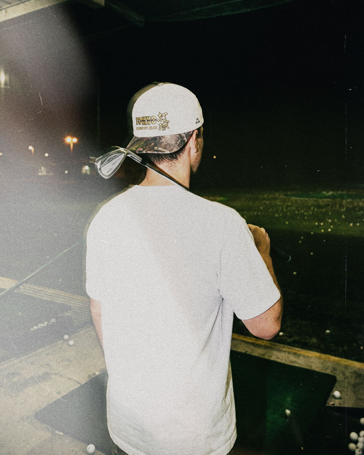 A man wearing a natural snapback cap with a camo brim and gold embroidery on the back.