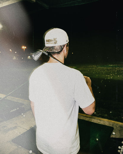 A man wearing a natural snapback cap with a camo brim and gold embroidery on the back.