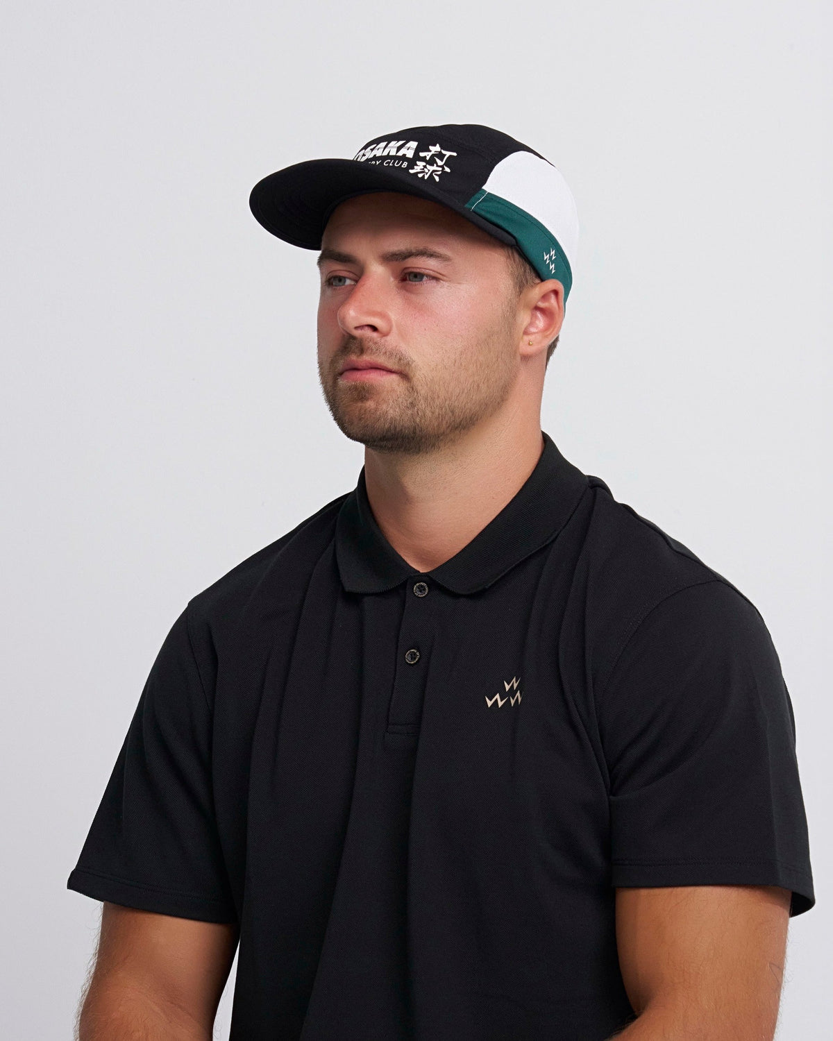 A man wearing a black, green, and white 8-panel sports cap with a printed front graphic design.
