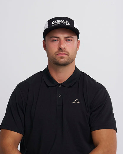 A man wearing a black and white sports cap featuring an Osaka Country Club printed graphic.