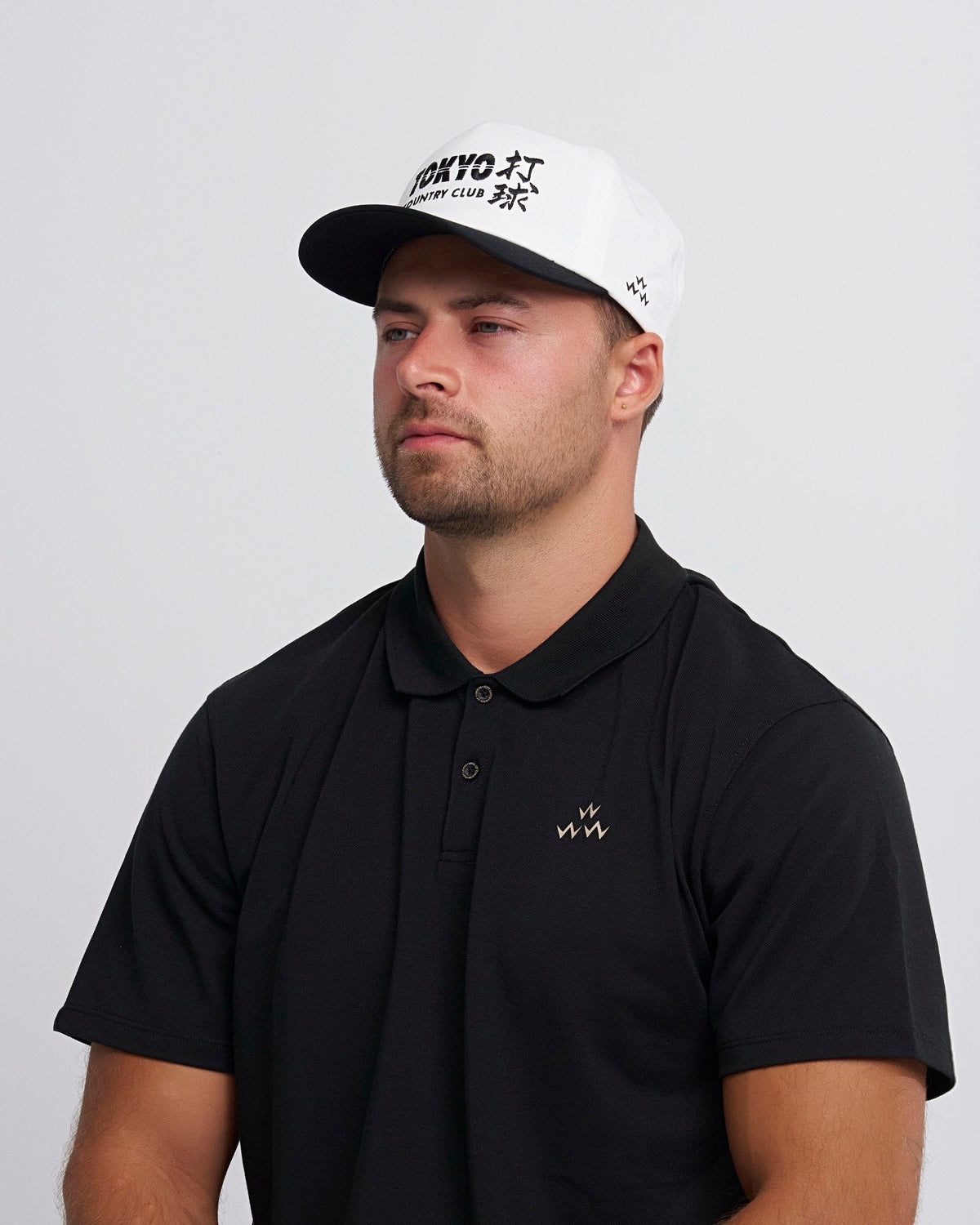 A man wearing a white snapback hat with a black brim and black text, and a black polo shirt.