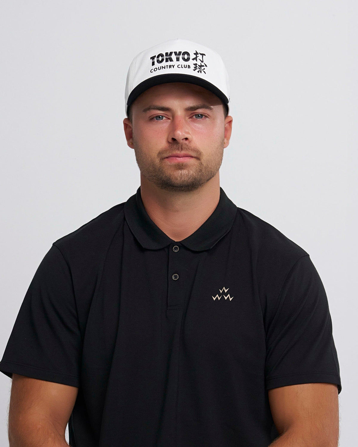 A man wearing a white snapback hat with black brim and Tokyo Country Club front embroidery.