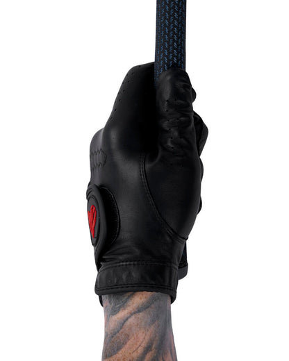A hand wearing a black leather golf glove with a red heart logo, gripping a textured golf club.