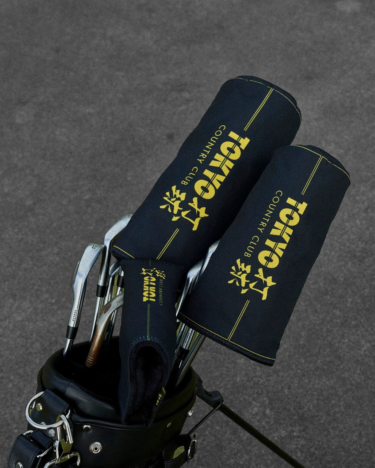 Two black headcovers with gold Tokyo Country Club text and line details in a golf bag.