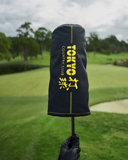 A black golf headcover featuring yellow vertical text and Japanese kanji motifs against a green course.