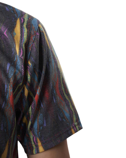 Detail of a Coogi print polo shirt with a colourful abstract pattern and a white script logo.