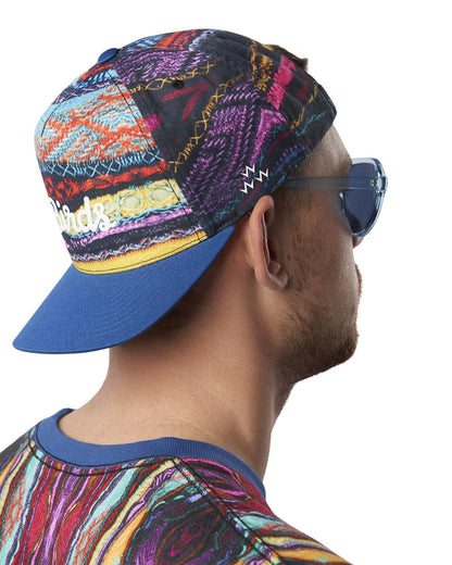 A man wearing a colourful Coogi print snapback hat with a blue peak and white script logo.