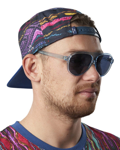 A man wearing a Coogi print snapback with a dark blue plastic back strap and translucent sunglasses.