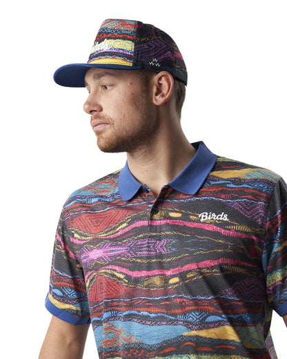 A man wearing a Coogi print cap with a blue peak and matching patterned polo.