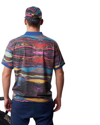 Back of a man wearing a multicolored Coogi print cap, matching polo shirt, and blue trousers.