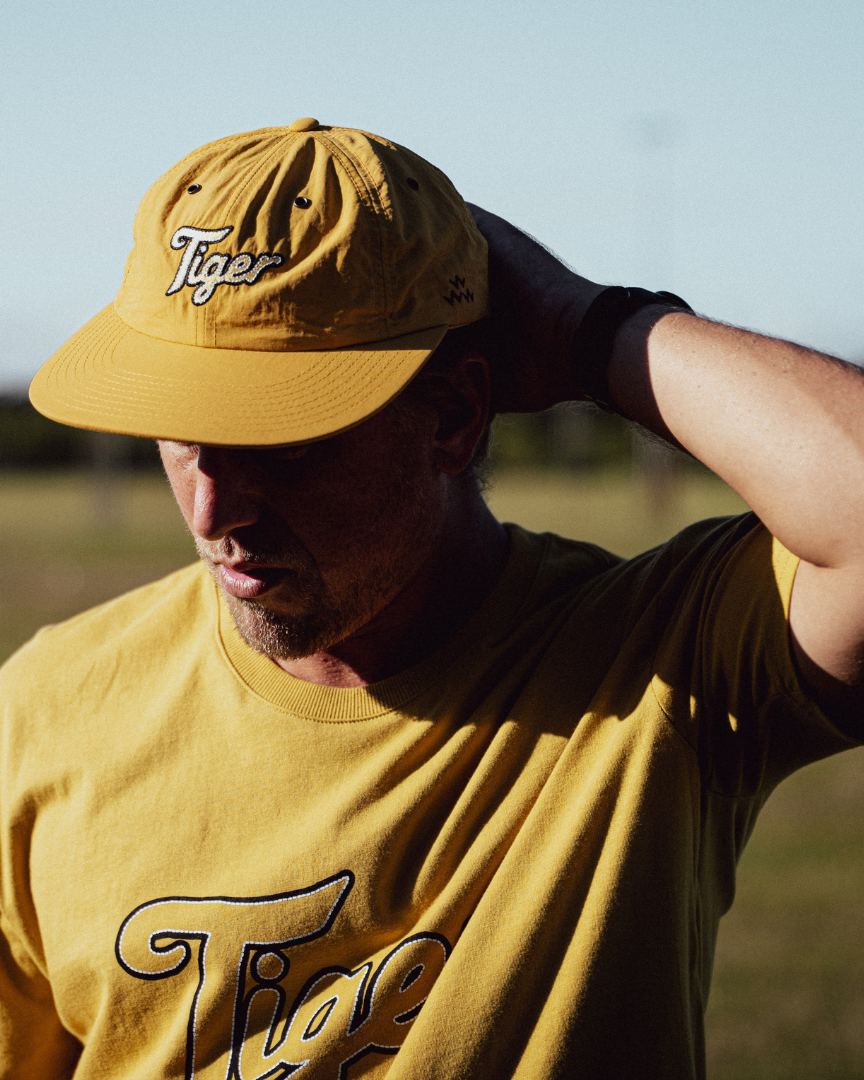 A person wearing a mustard strapback cap and matching t-shirt with embroidered Tiger logos.