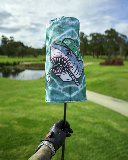 Teal tie-dye headcover featuring a shark graphic wearing a cap and holding a golf club on a course.
