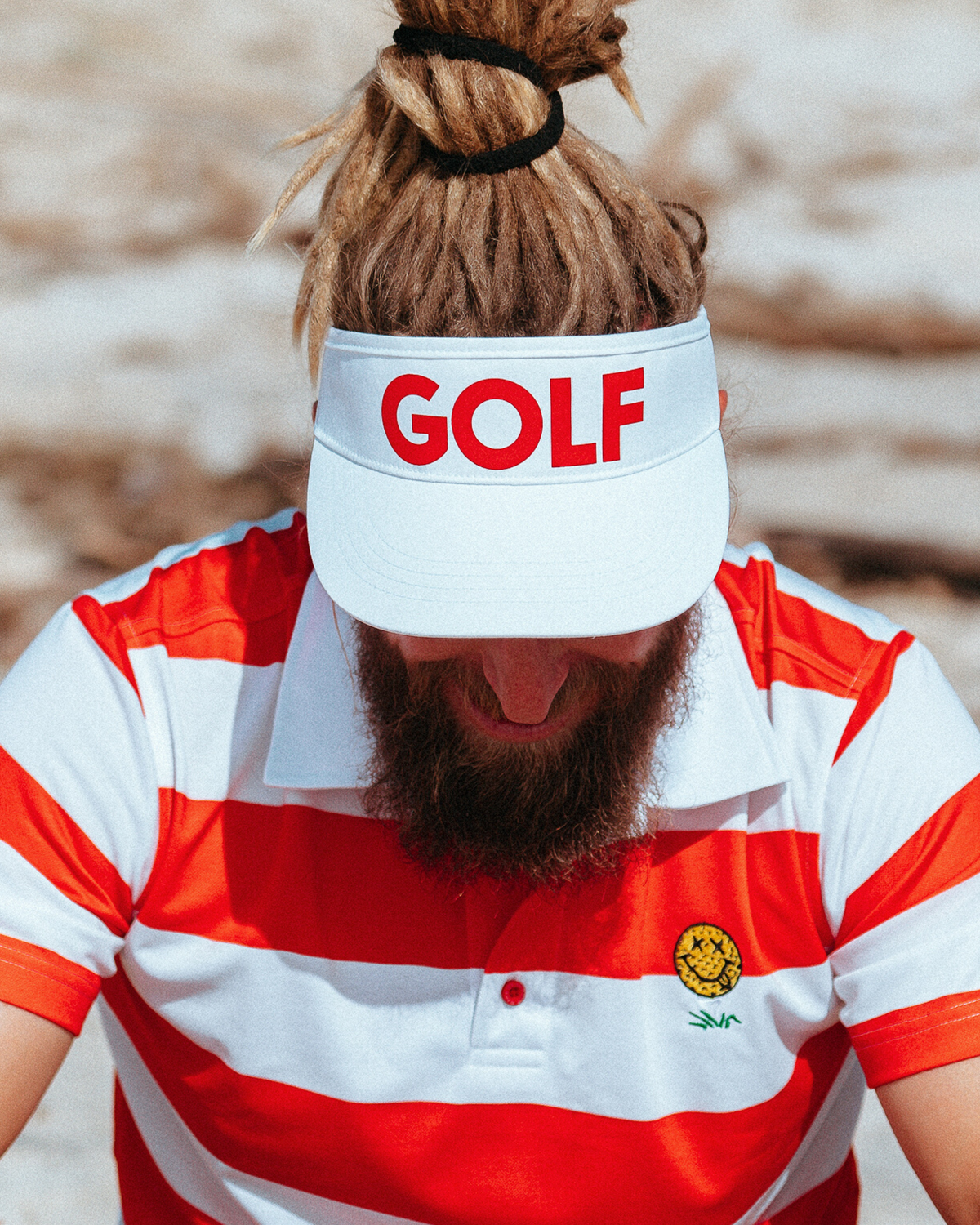 A person wears a white golf visor featuring bold red GOLF text across the front panel.